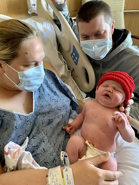 Father and Mother wearing masks and holding newborn Baby