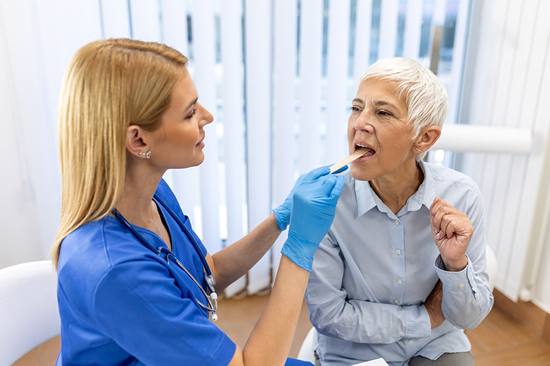 Speech Language Hearing Female nurse in blue scrubs inspecting the tongue of an older woman